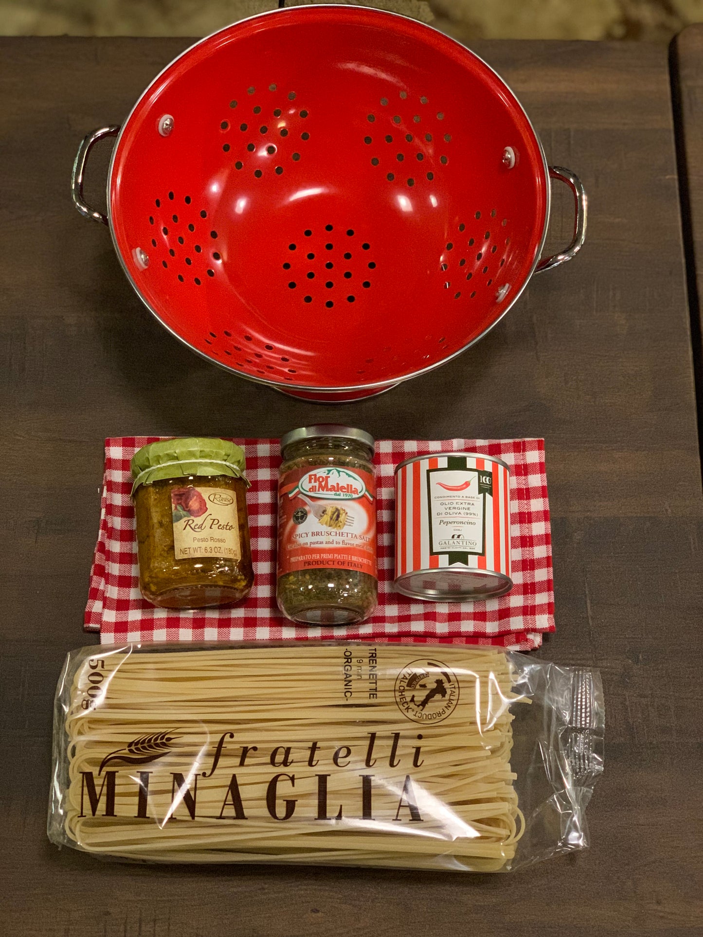 Red colander, jars of pasta sauce, and a package of Fratelli Minaglia pasta on a wooden surface.